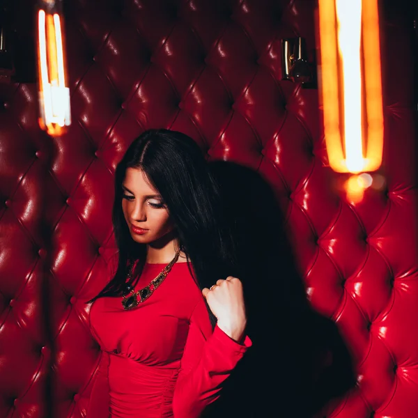 Ung kvinna i röd klänning står nära väggen — Stockfoto