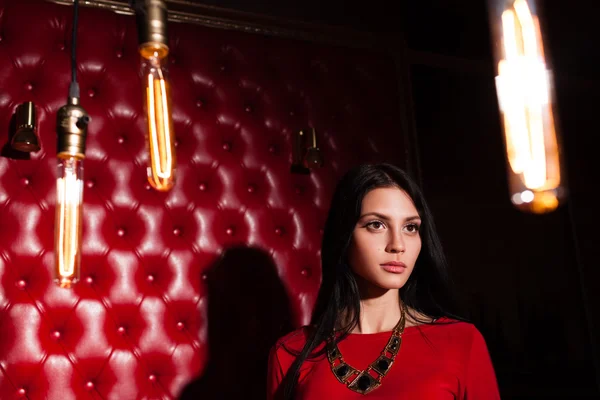 壁の近くに立つ赤いドレスの若い女性 — ストック写真