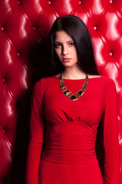 Jovem mulher em vestido vermelho de pé perto da parede — Fotografia de Stock