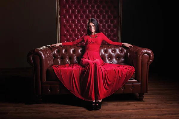 Young woman in red dress sitting on leather sofa — Stock Photo, Image