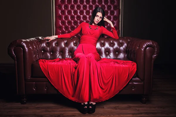 Young woman in red dress sitting on leather sofa — Stock Photo, Image