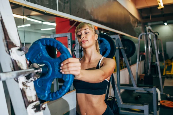 Athletic girl sets weight on barbell in the gym — ストック写真