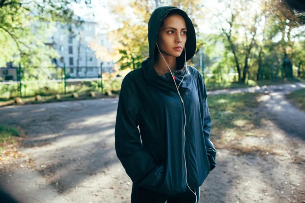 Sporty woman wearing hood jacket and listening music — Stock Photo, Image