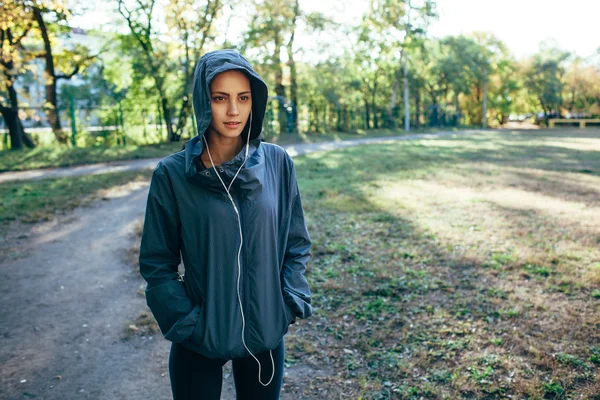 Sportovní žena nosí kapuci bundu a poslech hudby — Stock fotografie