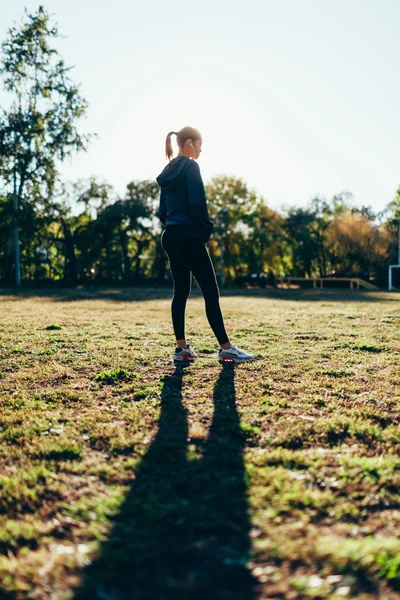 Mujer de pie en el patio deportivo contra el sol — Foto de Stock