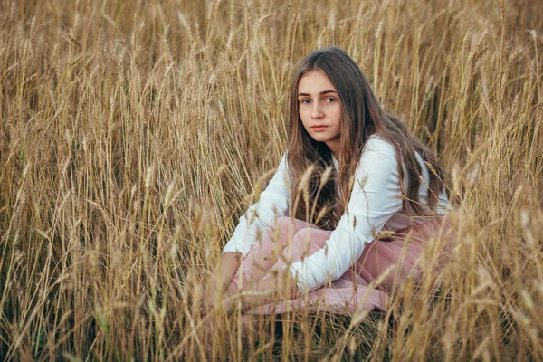 Jovem mulher vestindo vestido sentado em campo com trigo — Fotografia de Stock