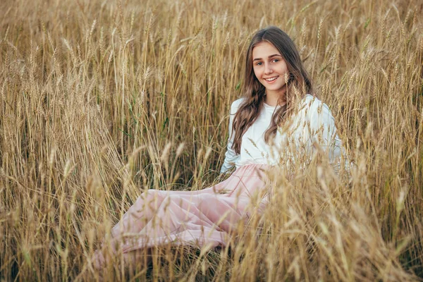 Jovem mulher vestindo vestido sentado em campo com trigo — Fotografia de Stock