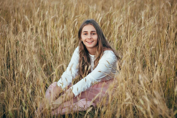 Jovem mulher vestindo vestido sentado em campo com trigo — Fotografia de Stock