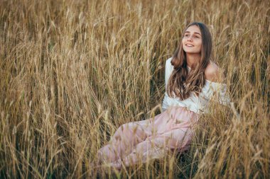 Buğday alanı oturan genç kadın giyiyor elbise