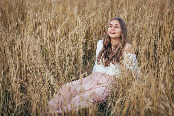 Ung kvinna bär klänning sitter i fält med vete — Stockfoto