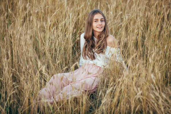 Mujer joven con vestido sentado en el campo con trigo — Foto de Stock