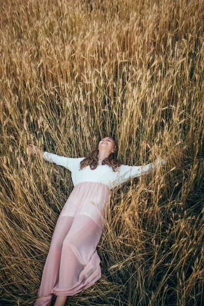 Mladá žena nosit šaty leží v oblasti s pšenice — Stock fotografie