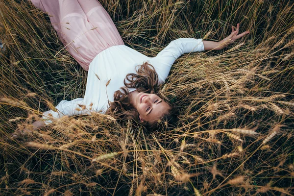 Jovem mulher vestindo vestido deitado no campo com trigo — Fotografia de Stock