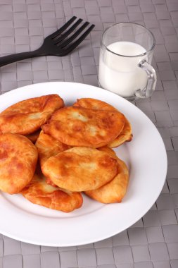 Kızarmış kek beyaz tabak, çatal ve gri hasır üzerinde süt fincan 