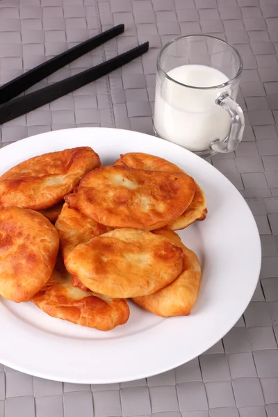 Bolos fritos em placa branca, pinças de cozinha e xícara de leite em gra — Fotografia de Stock