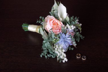 Düğün buketi suni çiçekler ve alyanslar loş ışıkta karanlık bir masada. 