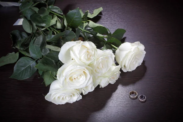 Bouquet of white roses and wedding rings on a dark table