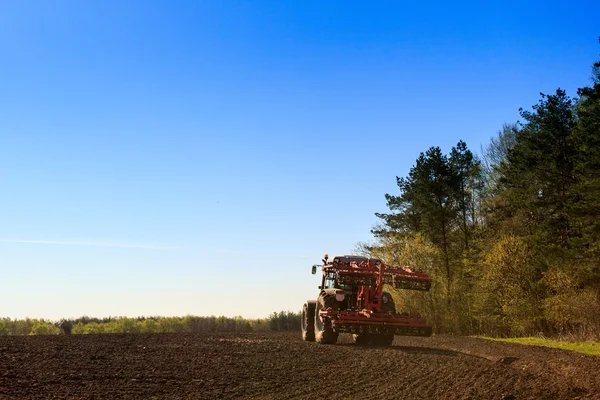 Backside view cultivator on ploughed field by spring wood — Stock Photo, Image