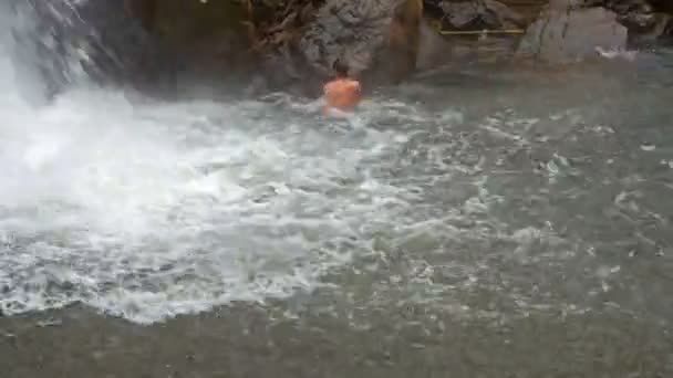 Mann schwimmt Glücksspiel unter schäumendem Wasserfall — Stockvideo