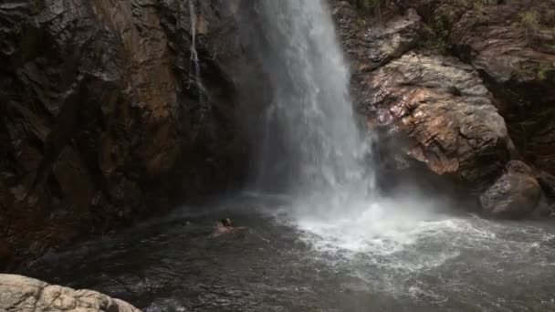 Mann schwimmt Glücksspiel unter schäumendem Wasserfall — Stockvideo