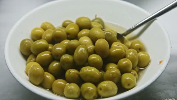 Top view closeup σε μικρό άσπρο μπολ με μαριναρισμένες πράσινες ελιές σερβιρισμένες με κουτάλι — Αρχείο Βίντεο
