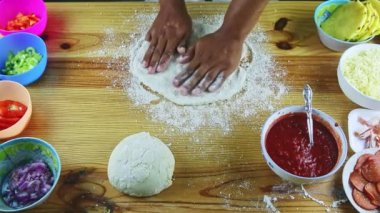 Manzaranın zirvesinde pizza hamurunu ahşap masanın üstünde büyük ve ince yapan adam var.