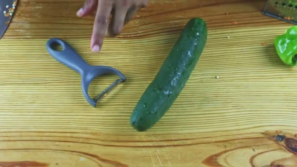 Bovenaanzicht op mensenhanden schillen grote rijpe groene komkommer door speciale peeler mes — Stockvideo