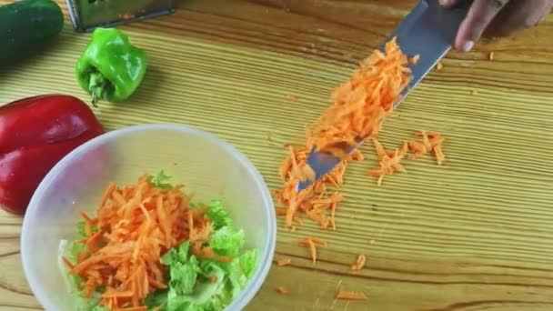 Shora pohled na člověka ruce nožem klade strouhanou mrkev do plastové mísy se salátem — Stock video