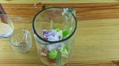 İnsan ellerinin üst görüntüsü blender kadehinin yanında servis edilen küçük bardağa su döker.