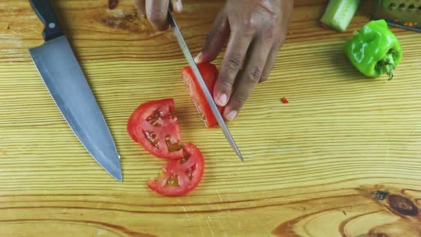Вид сверху на руки человека большим ножом нарезать большой спелый красный помидор на куски — стоковое видео