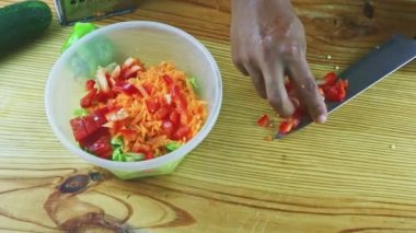 Bıçakla insan elinin üst görüntüsü küçük kırmızı biber parçalarını salata kasesine koy.