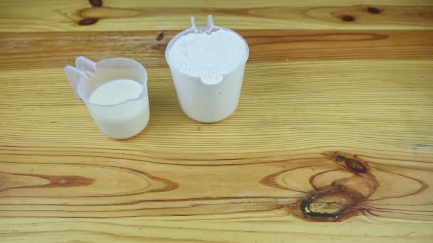 顶部的两个开放的塑料壶，与面粉和牛奶一起放在木制桌子上 — 图库视频影像
