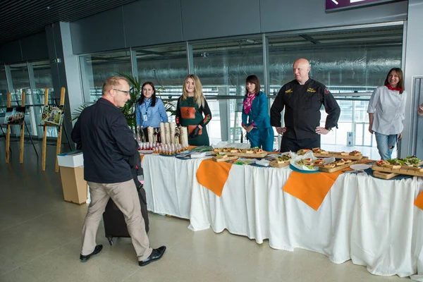Chef-koks in verschillende uniformen serveren snacks op tafel voor degustatie in Lviv Airport Hall Stockfoto