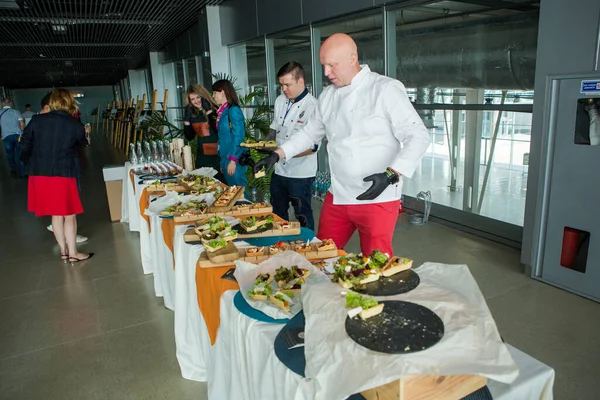 Chef-koks in verschillende uniformen serveren snacks op tafel voor degustatie in Lviv Airport Hall Stockafbeelding