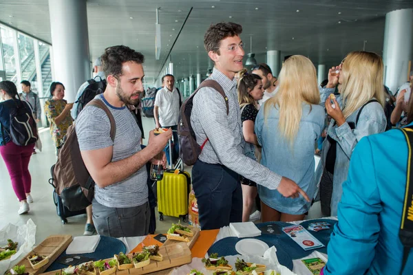 Primer plano pasajeros probar bocadillos y bebidas de la mesa de degustación gratuita en la sala del aeropuerto de Lviv Imagen de archivo