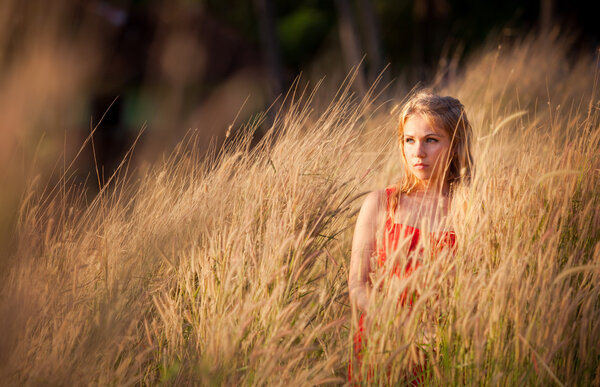Girl in red dress with long blonde hair stand in golden field on sunset light