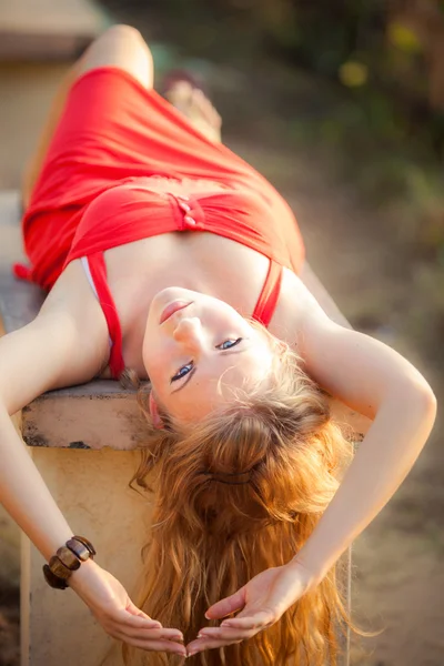 Menina loira em vestido vermelho colocar no banco — Fotografia de Stock