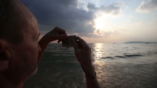 Зрелый мужчина на пляже с камерой — стоковое видео