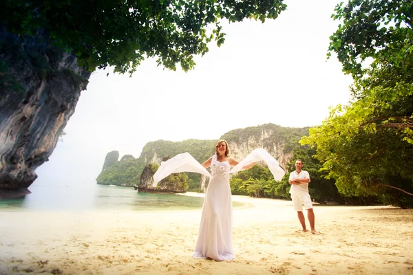 Bride and groom stand on sand beach barefoot near green trees — Stock Photo, Image