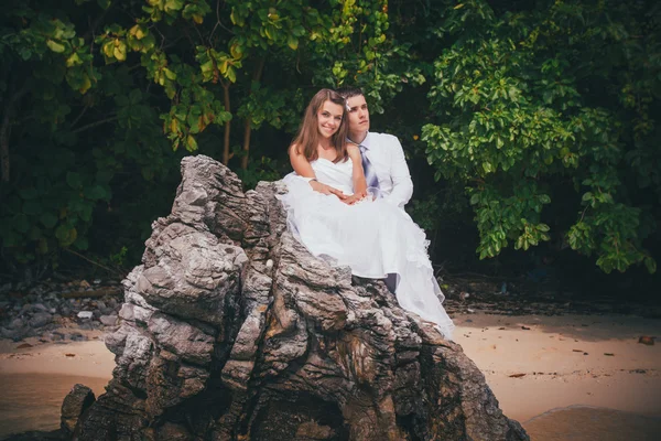 Jonge bruid en bruidegom zitten op rots — Stockfoto