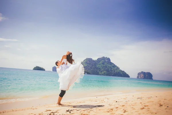 Groom lifts bride up at sand beach — Stock Photo, Image