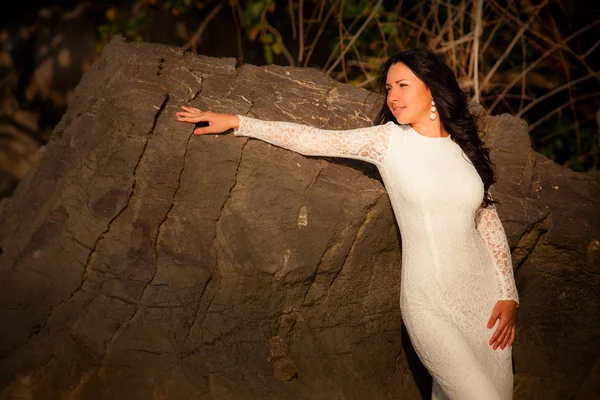 Bruid leunt tegen rots op strand — Stockfoto