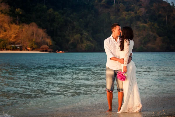 Bruden och brudgummen promenad på stranden i gryningen — Stockfoto