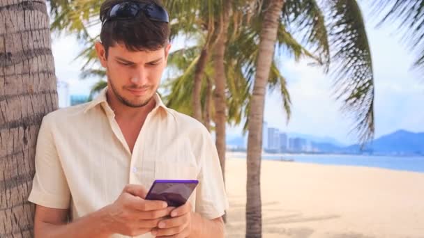 Jovem com telefone sob palmeira — Vídeo de Stock