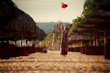 slim girl in long throws up big red hat among reed umbrellas