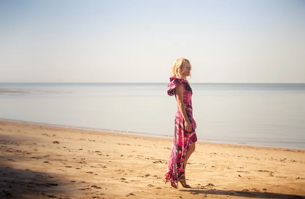 紫色のドレスでブロンドの女の子がビーチを歩く — ストック写真