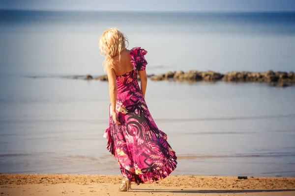 Blondýnka v purpurových šatech chodí na pláži — Stock fotografie