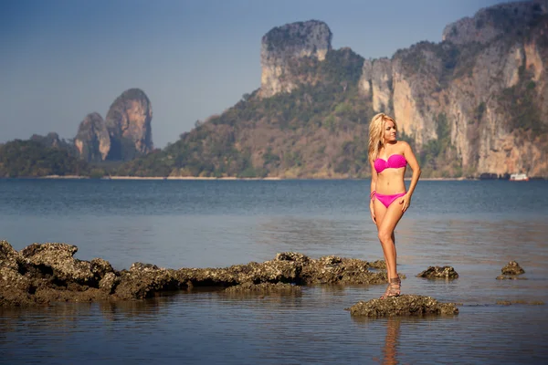 Blond tjej i baddräkt stå på havet stenar — Stockfoto