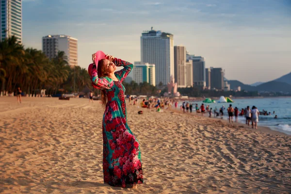 Schlankes Mädchen mit langem und großem Hut blickt auf die Sonne am Strand in der Stadt — Stockfoto