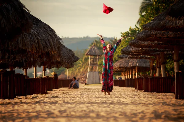 slim girl in long throws up big red hat among reed umbrellas
